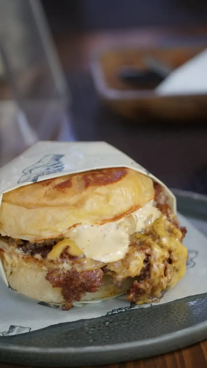 Close view of a smash burger with melted cheese, pickles and sauce