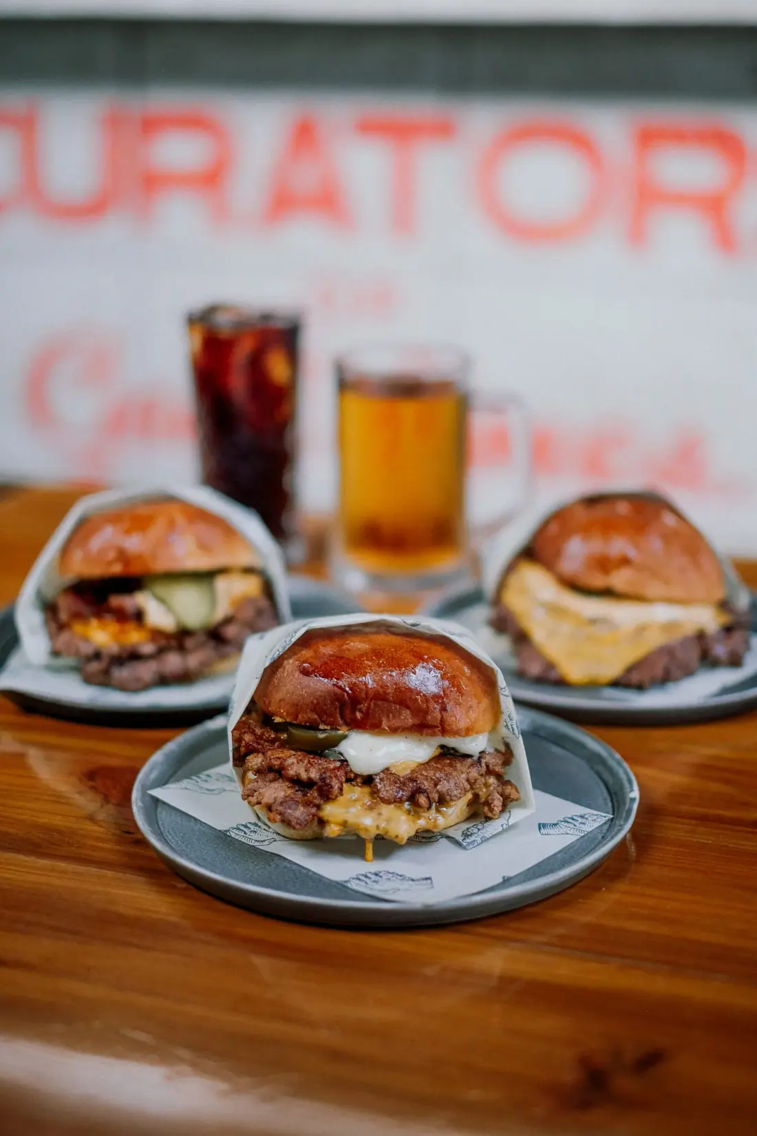 Three smash burgers with fries, a cola and a beer on a wooden table
