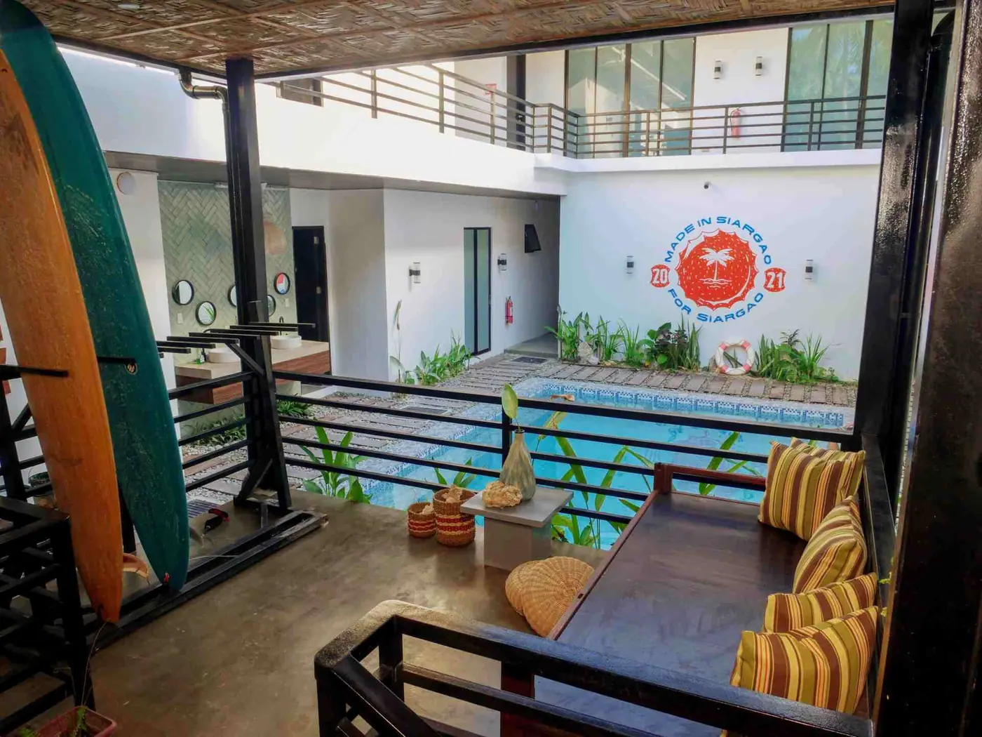 Courtyard pool with rooms around it and a surfboard leaning on the upper walkway