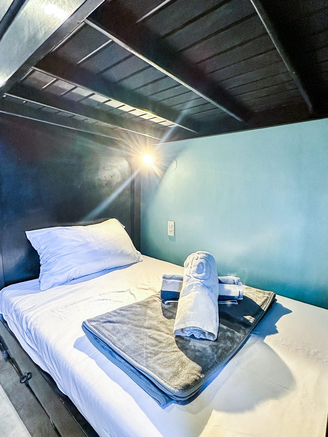 The foot of the dorm bunks, with a ladder, a curtain and a wall air conditioner